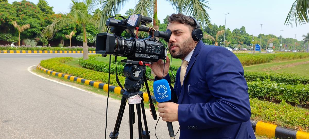 Dr. Sari Hamoud checking a shot through a broadcast camera on a tripod during G20 coverage
